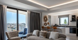 Una sala de estar moderna con un sofá, sillones y vistas a la ciudad a través de amplios ventanales.