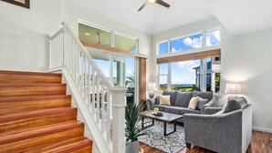 A spacious living area with a staircase, a gray sofa set, and large windows offering a view of the outdoors.