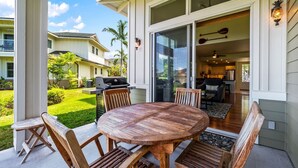 A wooden dining table with chairs on a covered patio with a view of a backyard and neighboring houses.