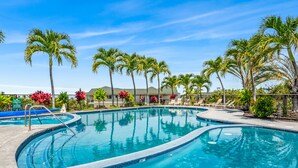A swimming pool with a curved design, surrounded by palm trees and lounge chairs.