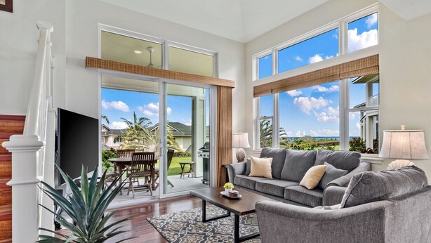 A spacious living room with a grey sofa, a coffee table, and a large window offering a view of the outdoors.