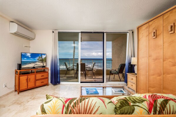 Un salón con televisión, un sofá, una mesa de centro y vistas a la playa a través de un ventanal corredero.