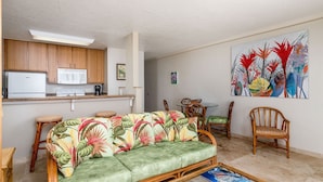 A living room with a sofa, chairs, a dining table, and a kitchen area with a refrigerator and microwave.