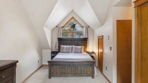 A bedroom with a sloped ceiling, a wooden bed, a nightstand, a lamp, and a wardrobe. - Near Hot Springs + Downtown Ouray | Deck with Views (Ouray)