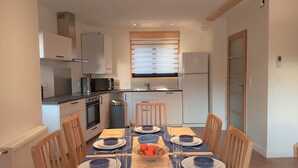 Une cuisine compacte dotée d’appareils électroménagers modernes, une table à manger pour quatre personnes et une petite poubelle.