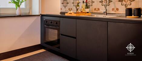 A modern kitchen with dark cabinetry, a tiled backsplash, and a window with a plant.