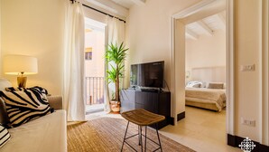 A modern hotel room with a sofa, a TV, a dining table, and a potted plant.