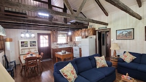 L’intérieur d’un chalet rustique comprend un coin repas, une cuisine et deux canapés bleus agrémentés de coussins à motifs floraux.