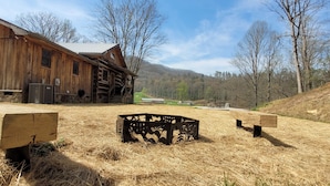 Une grange rustique en bois, surmontée d’un toit en métal, entourée d’un champ aride et herbeux et d’arbres sans feuilles.