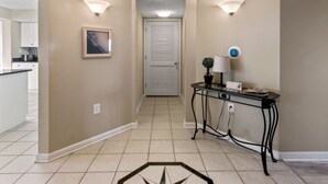 A hallway with beige walls, a framed picture, a potted plant, a table with a lamp, and a thermostat. - Yacht Club Villas #1-1005 Beautiful Waterfront Villa in Barefoot Resort! (North Myrtle Beach)