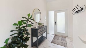 A hallway with a black console table, a large mirror, a potted plant, a door with a glass panel, and a wall-mounted light fixture. - Poolside Bliss and a Family-Friendly Oasis (Naples)