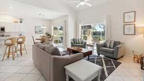 A modern living room with a sofa, coffee table, and chairs, a kitchen area with white cabinets, and a dining space with a table and chairs. - Poolside Bliss and a Family-Friendly Oasis (Naples)