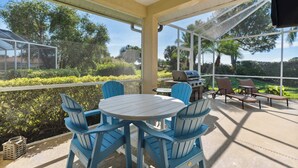 A covered patio with a table and chairs, a grill, and a view of the surrounding greenery. - Poolside Bliss and a Family-Friendly Oasis (Naples)
