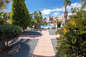 A pathway leading to a pool surrounded by tropical plants and a clear blue sky.
