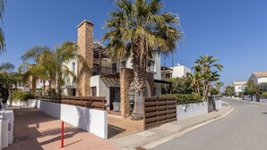 A modern residential building with a stone facade, palm trees, and a clear blue sky.