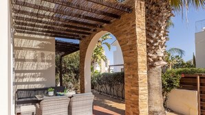 A covered patio with wicker furniture, a pergola, and a view of a white building in the background.