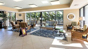 Eine geräumige Lobby mit Rattanmöbeln, großen Fenstern und einem blauen, gemusterten Teppich.