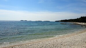 Een strand met helder water, een kiezelstrand en verre eilanden.