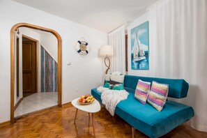 A living room with a teal sofa, a small white table with fruit, a lamp, and a painting of a sailboat. - Sorgenfrei 2-bedroom apartment in Rovinj Old Town (Rovinj)