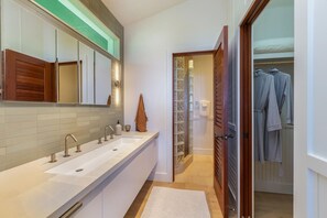 A modern bathroom with a large sink, mirror, and wooden door leading to a walk-in closet. - Camp Alealea 2 3 Bedroom Home by RedAwning (Hanalei)