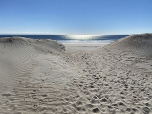 Una spiaggia sabbiosa con impronte che conducono verso l'acqua, un cielo sereno e l'oceano sullo sfondo.