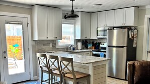A kitchen with white cabinets, a stainless steel refrigerator, and a large island with bar stools. - Great location! Fully fenced in yard and expansive deck. Come and relax! (Oak Island)