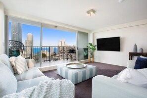 A modern living room with a large balcony, a flat-screen TV, and a view of the city skyline. - Relax with Beach and River views in 3br apt w/pool (Surfers Paradise)