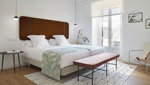 Un dormitorio moderno con una cama grande, mesitas de noche, un banco y vistas al exterior a través de amplios ventanales.