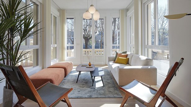 Un salón luminoso con un gran ventanal, un sofá, una mesa de centro y dos sillones.