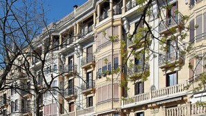 Un edificio de varios pisos con balcones, fachada de piedra y un cielo azul despejado.