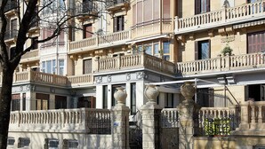 Un edificio de varios pisos con balcones, barandillas ornamentales y una entrada con portón.