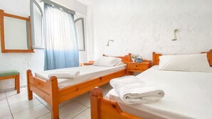 A room with two wooden beds, a small table, a chair, and a window with curtains. - Maria Apartments (Hersonissos)