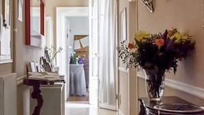 Ein Flur mit Fliesenboden, einem Holztisch mit Blumenvase und einem Spiegel an der Wand.