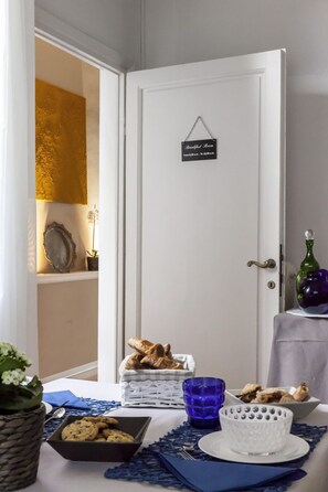 Montaje para el desayuno con un cartel que indica los horarios del comedor, una cesta de pan, un plato con galletas y un vaso azul.