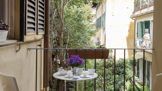 Ein kleiner Balkon mit zwei weißen Stühlen und einem Tisch, gedeckt mit Tassen und Tellern.
