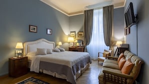 Ein Hotelzimmer mit einem großen Bett, zwei Nachttischen mit Lampen, einem Sofa, einem an der Wand montierten Fernseher und einem Fenster mit Vorhängen.