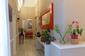 Un pasillo con una recepción blanca, plantas en macetas y un espejo.