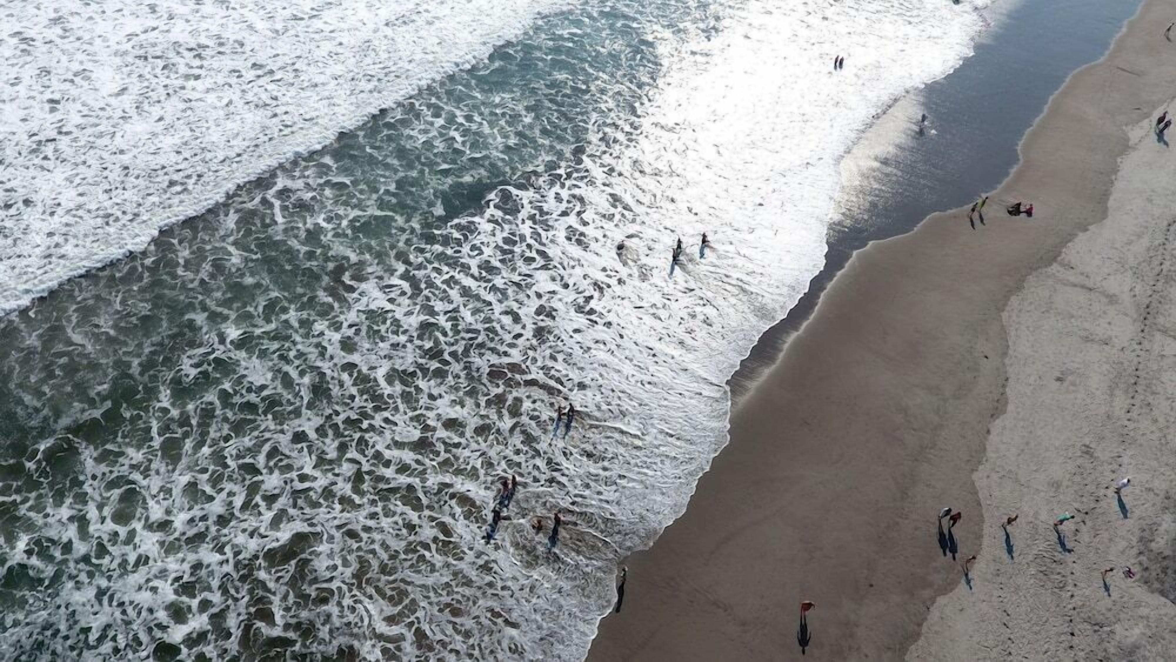 A beach with waves crashing onto the shore and people walking along the sand.