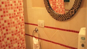 A bathroom with a checkered shower curtain, a towel rack with a white towel, a mirror with a patterned frame, and a soap dispenser. - Beer Hotel Iguazu Hostel (Puerto Iguazú)