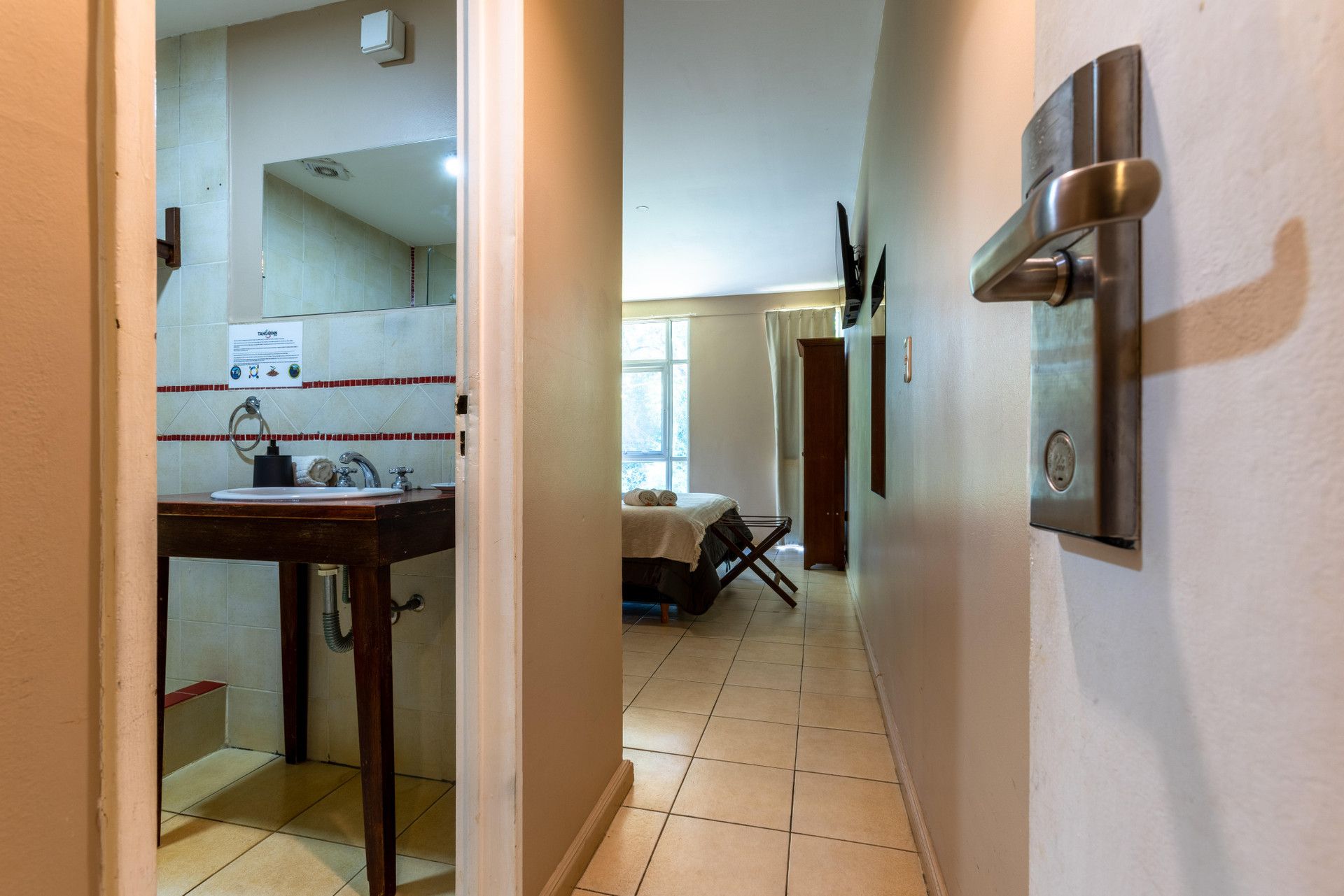 Un couloir menant à une salle de bain équipée d’un lavabo, d’un miroir et d’un porte-serviettes.