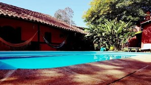 Une piscine avec une terrasse carrelée, un hamac et un bâtiment rouge avec un toit en tuiles.