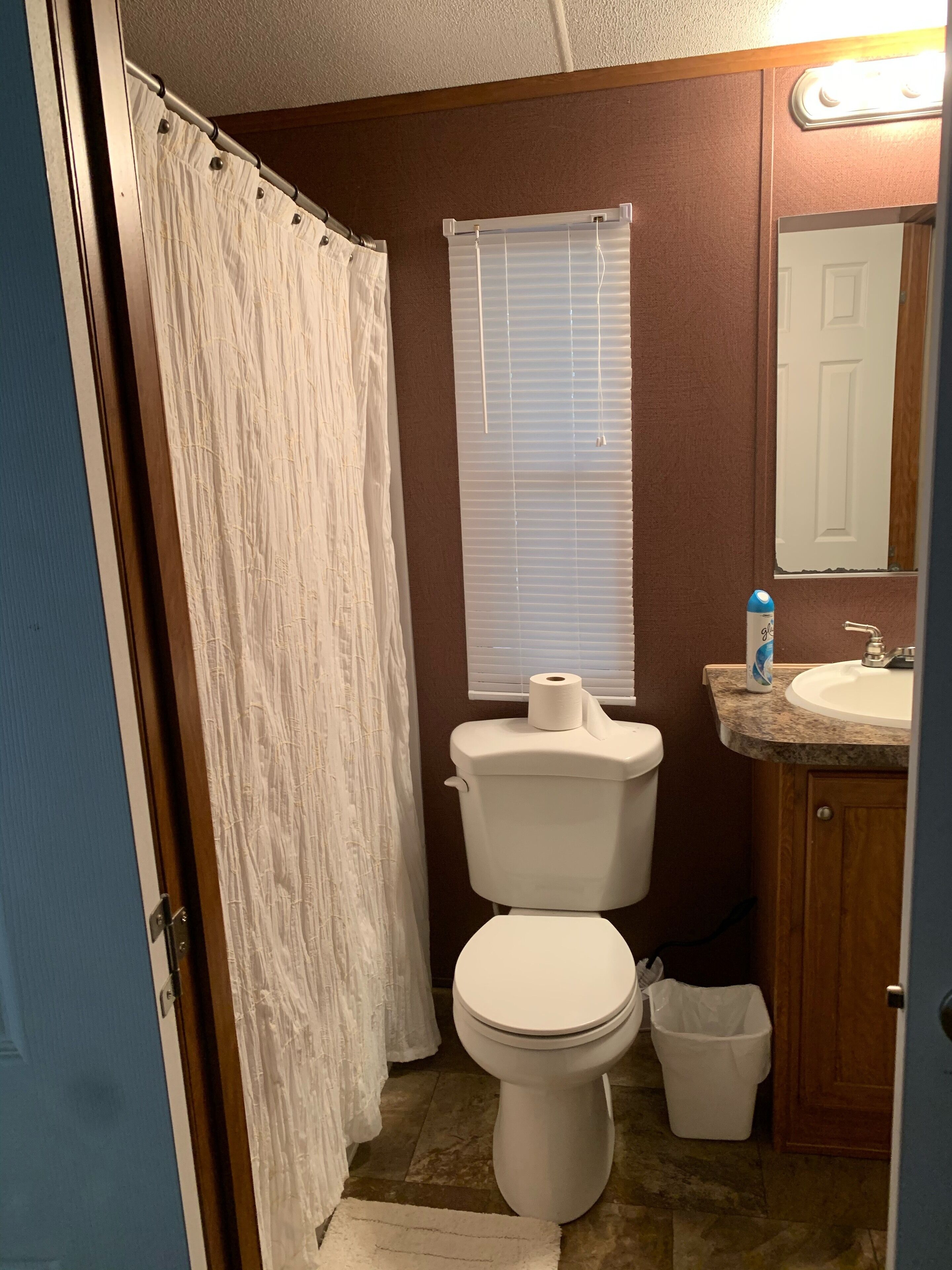 Ein Badezimmer mit Toilette, Waschbecken, Duschvorhang und einem Fenster mit Jalousien.