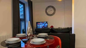 Et spiseområde med et rødt bord dækket til fire personer, en sort sofa og et ur på væggen.