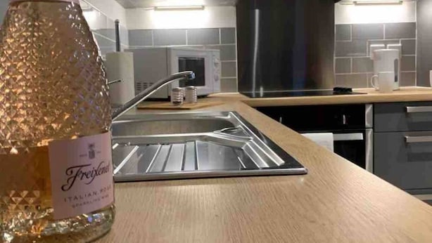 Et moderne køkken med en stålvask, en mikroovn og en flaske Freixenet danskvand på bordet.
