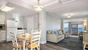 Un salón amplio con una mesa y sillas de madera, un sofá, y vista al mar a través de grandes ventanales.
