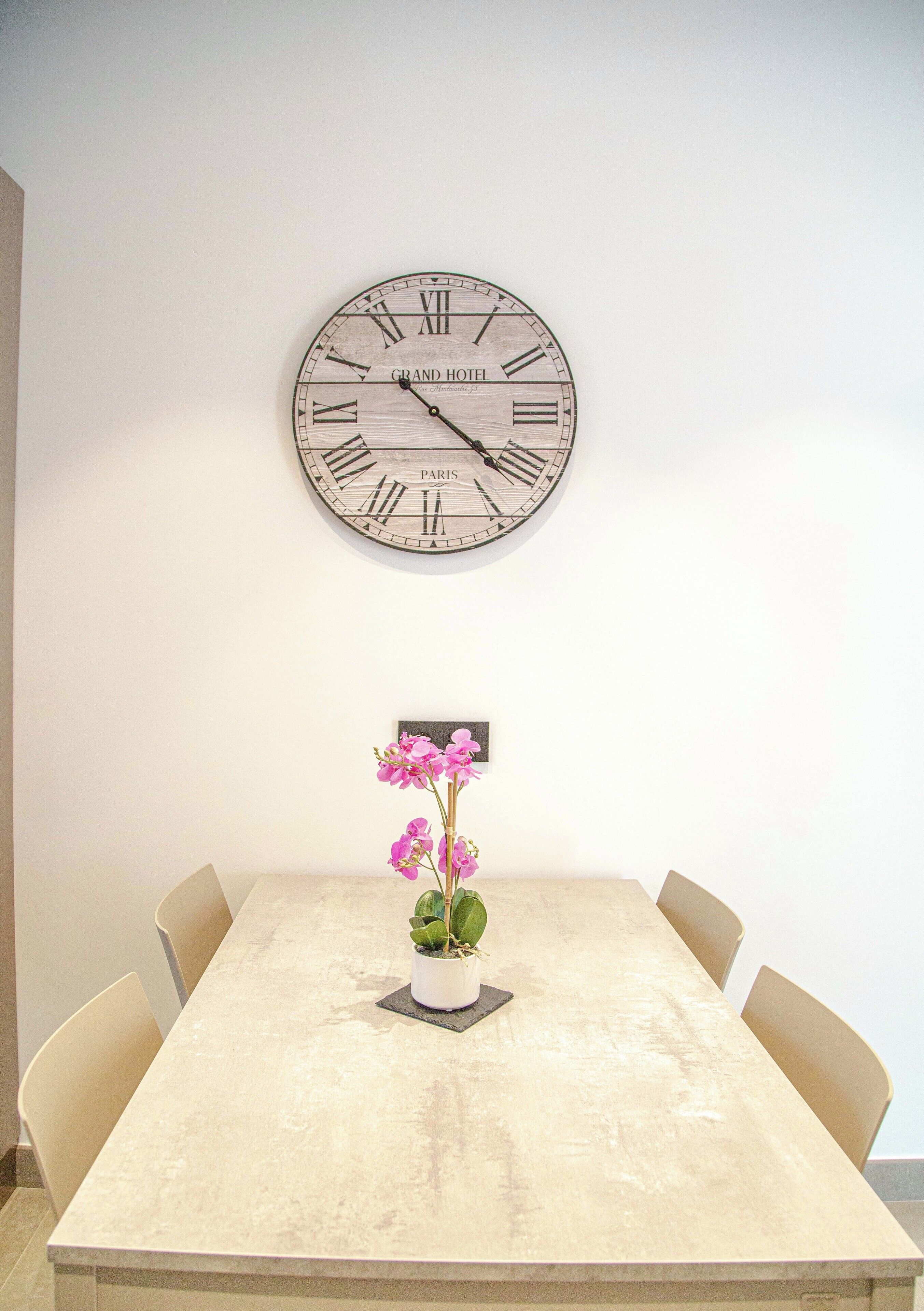 Ein Essbereich mit einem runden Tisch, vier Stühlen, einer Uhr und einer Blumenvase.