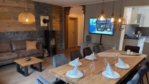A modern living room with a wooden dining table set for six, a sofa, and a TV mounted on the wall.