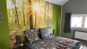 A bedroom with a bed, a chair, a window, and a wall mural.