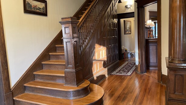 A wooden staircase with a handrail, leading to a landing with a rug and a door.