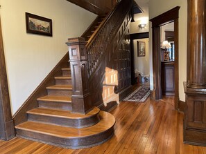 Un escalier en bois, doté d’une rampe, mène à un palier où se trouvent un tapis et une porte.